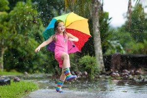 Young child playing in the rain wearing rain boots and holding an umbrella.