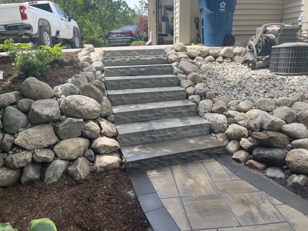 large boulder retaining wall with stone steps to a paver walkway