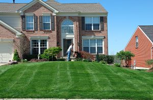 Two story brick house with large front yard with a lawnscaper mowing the grass. 