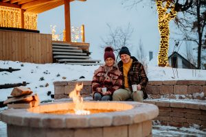 Senior couple sitting together on their outdoor patio, in front of a fire pit. 