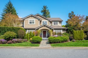 Two story home with a well landscaped front yard with green grass, trees, and shrubs. 