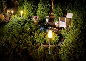 Illuminated home garden with patio plants, trees and a fountain 